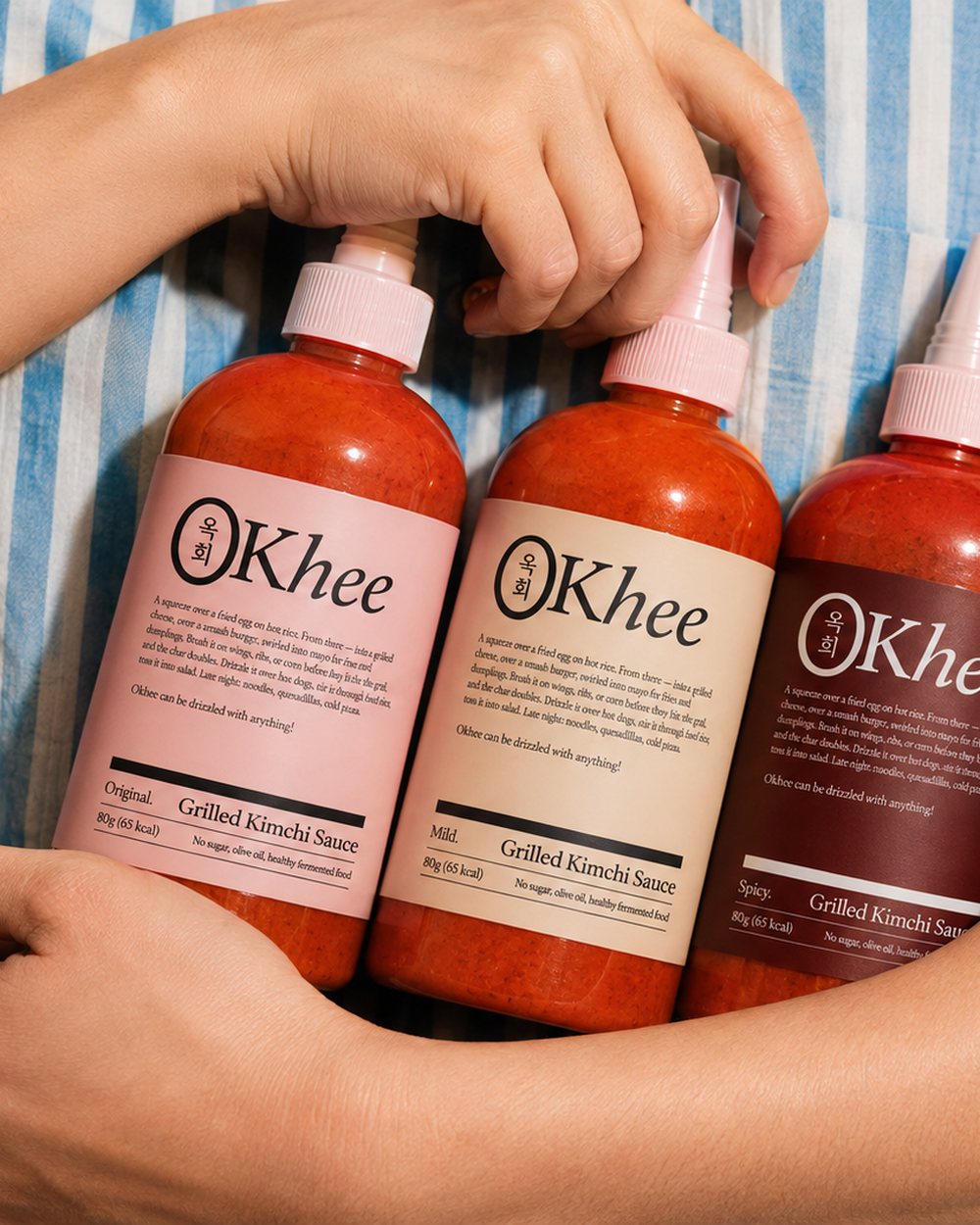 Three bottles of Okhee grilled kimchi sauce held in someone’s arms