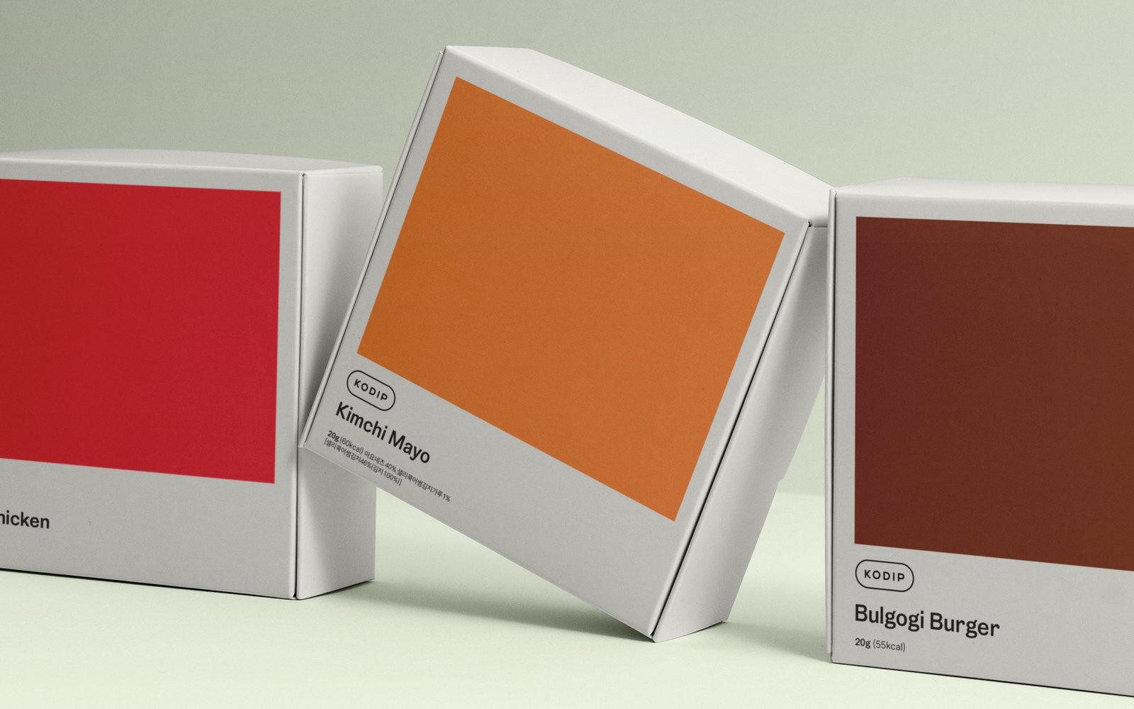 Three Kodip dip cartons in red, orange and maroon standing on a pale green surface