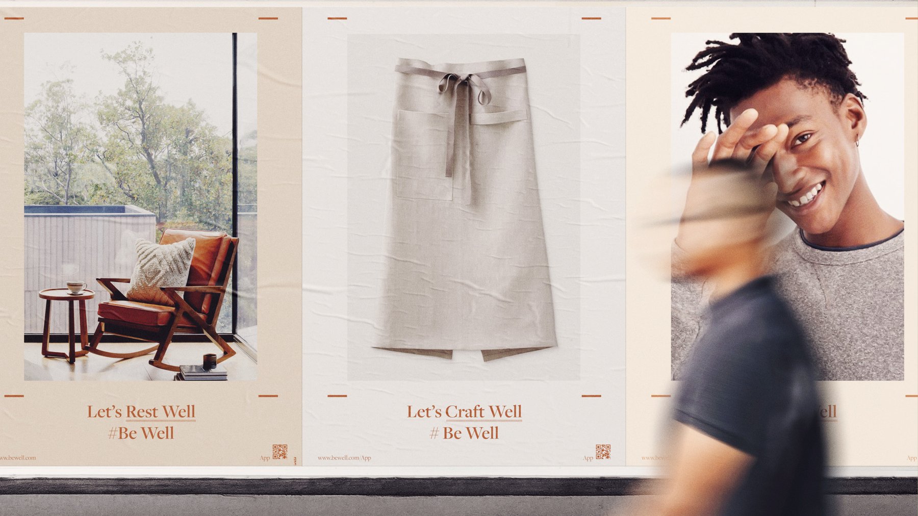 A street hoarding of Be Well posters — Let’s Rest Well, Let’s Craft Well — with a passer-by blurred in motion