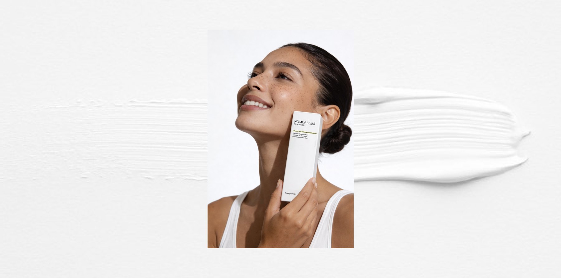 A woman holding a Nomorelies vitamin C serum carton beside her face, on a white textured ground