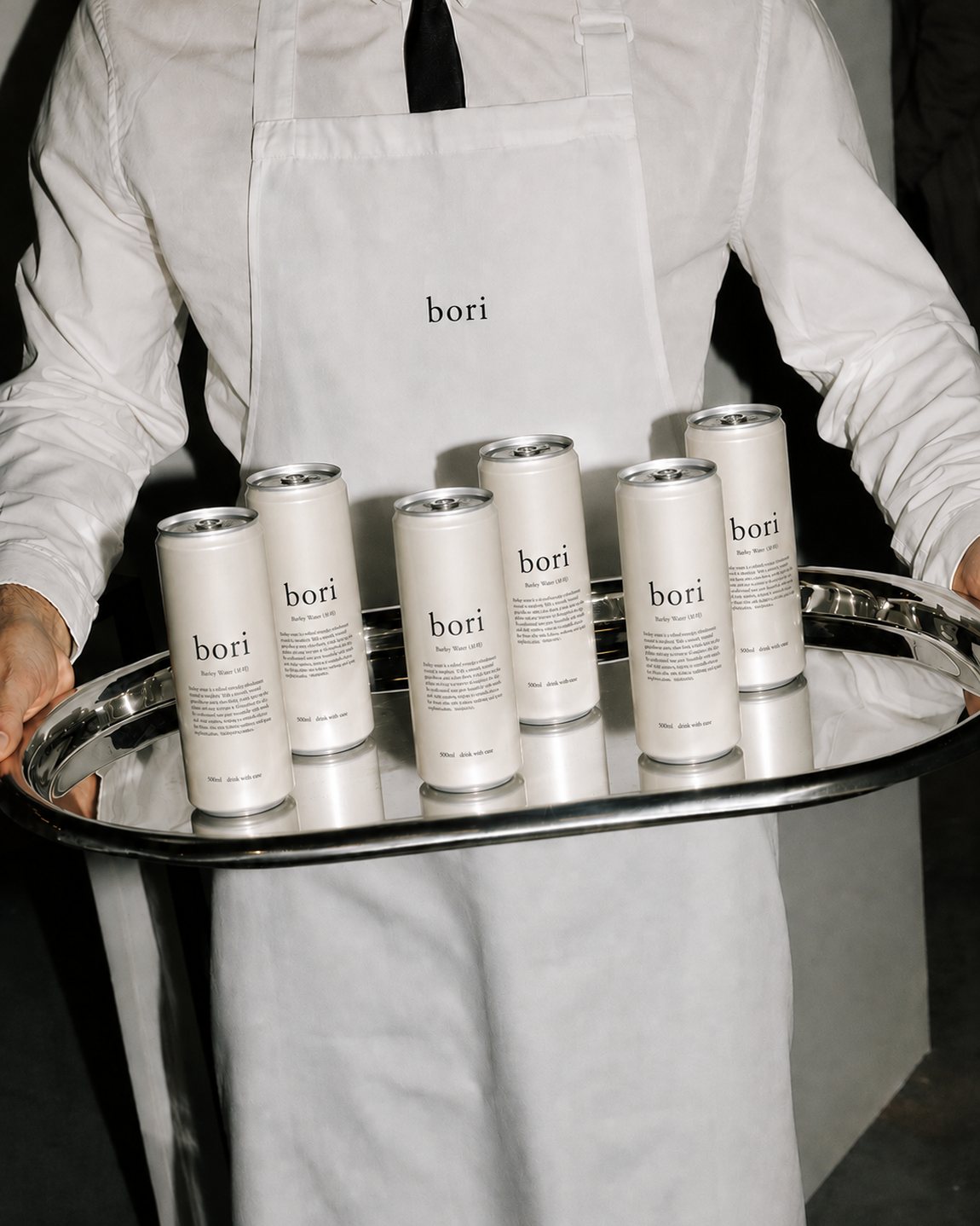 A server carrying a silver tray of Bori barley water cans