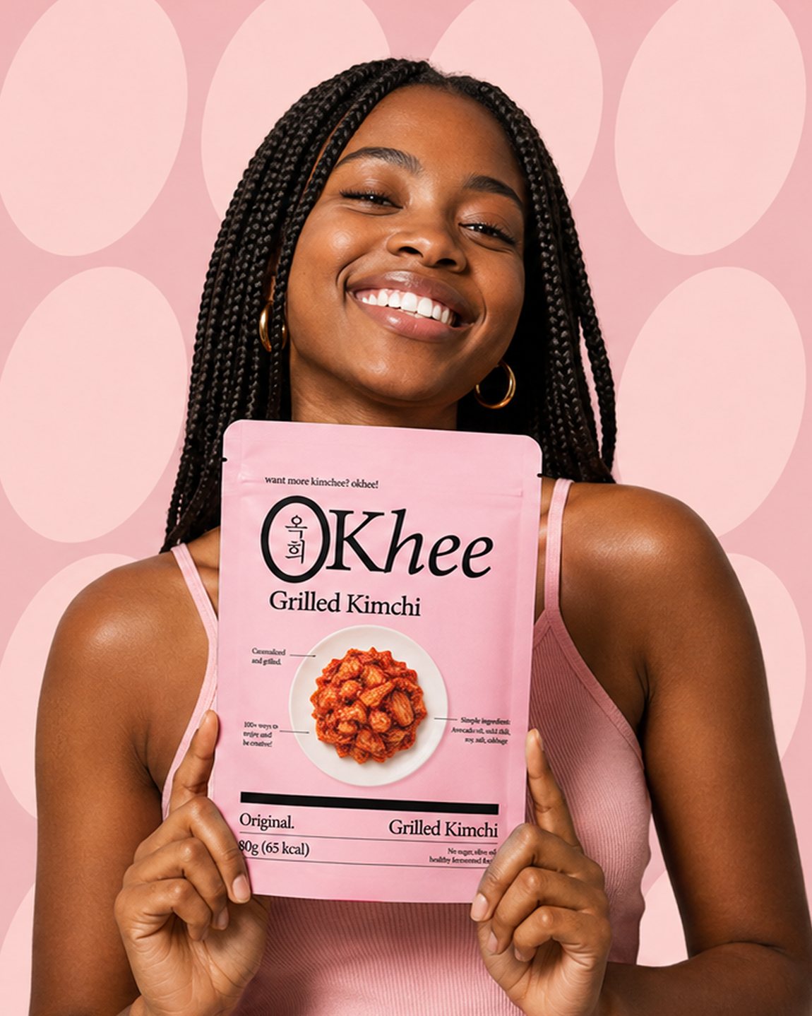 A smiling woman holding a pink Okhee Grilled Kimchi pouch against a pink patterned backdrop